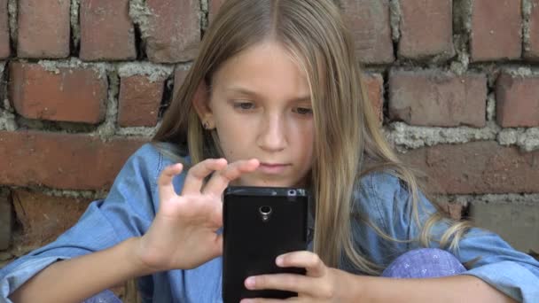 Criança usando Smartphone, Criança jogando no telefone inteligente, Menina ao ar livre no parque — Vídeo de Stock
