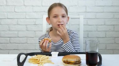 Çocuk fast food yiyor, çocuk restoranda hamburger yiyor, kız meyve suyu içiyor.