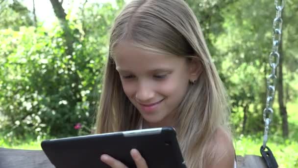 Дитина грає на планшеті гойдалки, дівчина використовує ПК на відкритому повітрі в природі, дитина в саду — стокове відео