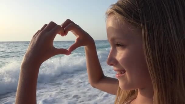 Ребенок играет на пляже, ребенок смотрит морские волны, девушка делает сердце формы знак любви — стоковое видео