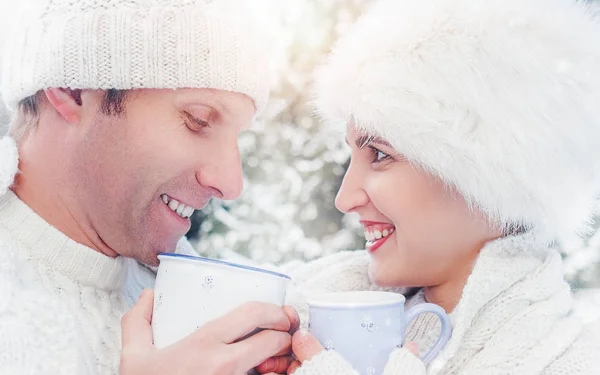 Cozy dressed couple drink hot tea on snow forest glade