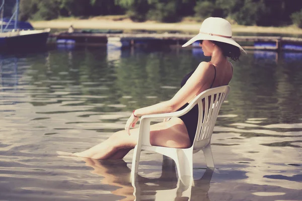Frau mit Sonnenhut sitzt auf Stuhl im Wasser — Stockfoto