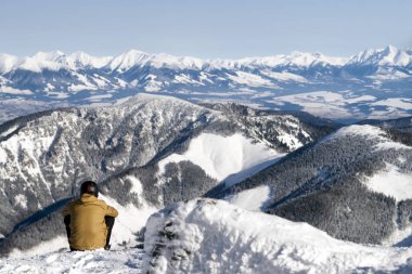 Man sitting on snow and looking on the winter hills 