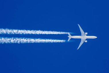 Boeing 777 mavi gökyüzünde uçuyor ve yoğunlaşma izi var.