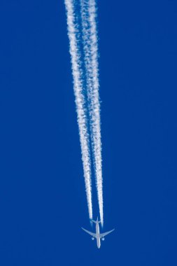 Boeing 777 mavi gökyüzünde uçuyor ve yoğunlaşma izi var.