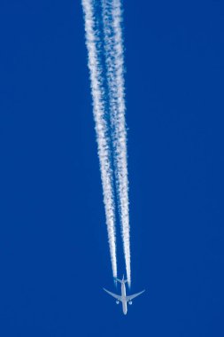 Boeing 777 in flight on blue sky and condensation trace clipart