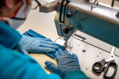 Terzi atölyedeki dikiş makinesinde koruyucu yüz maskesi yapıyor.