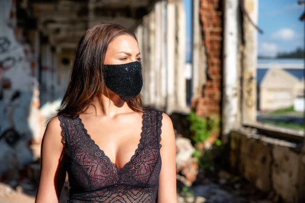 Woman with big breast at neckline in old factory building wearing luxury black fashion face mask due coronavirus Covid-19 protection