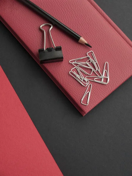 Office accessories: red notepad, black pencil, binder and paper clips on a black background. Top view. Copy space