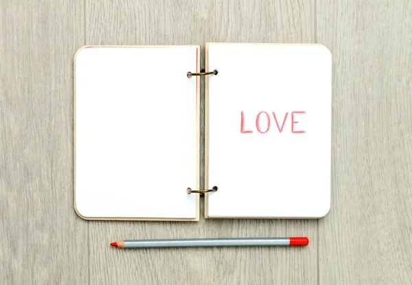 Opened blank notepad with drawn word LOVE on wooden table