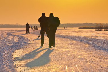 Güneş altında donmuş gölde buz patenciler