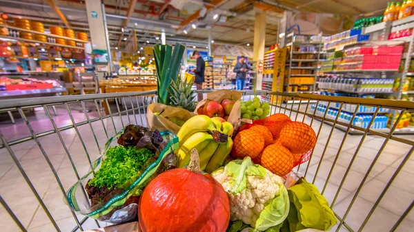 Supermarket trolley with people shopping in background — Stock Photo, Image