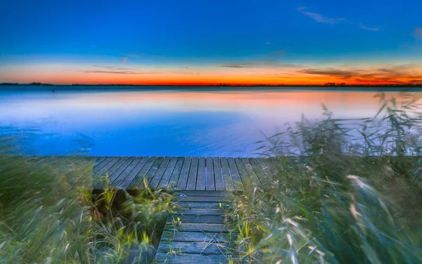 Imagem de exposição longa do por do sol azul e alaranjado sobre um cais no — Fotografia de Stock