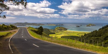 Inviting road through New Zealand countryside with blue sea clipart