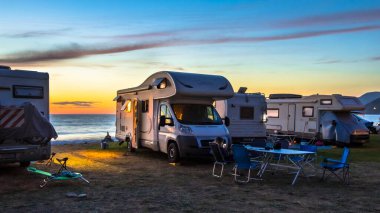 Campers and Motorhomes overlooking sunset in the Mediterranean sea from their campsite on the beach, Corsica, France clipart