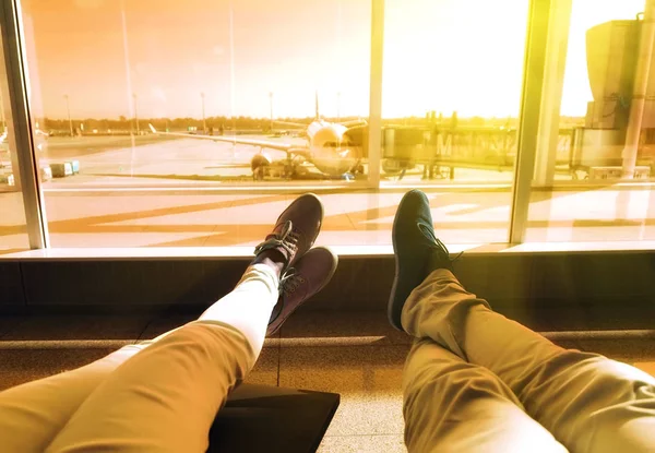 Pareja joven esperando el avión en un aeropuerto. piernas humanas con el avión en el fondo. Concepto de viaje — Foto de Stock