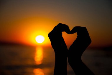 Gün batımı siluetiyle kalp şeklinde eller.