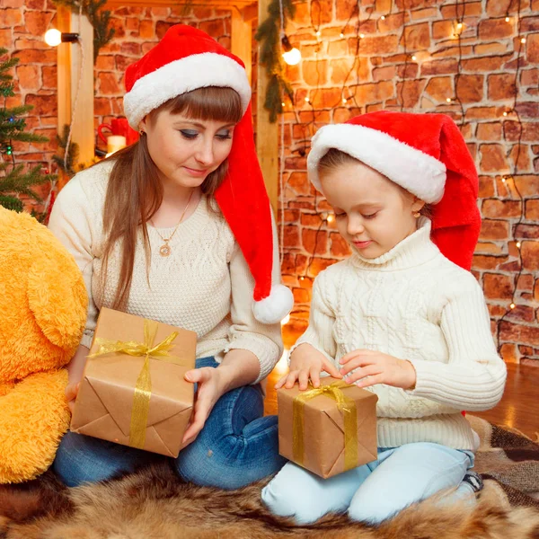 young mother with baby near Christmas tree in caps of Santa Claus