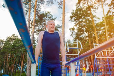 Parktaki paralel parmaklıklara triseps daldıran formda bir adam. Açık havada egzersiz yapıyor.