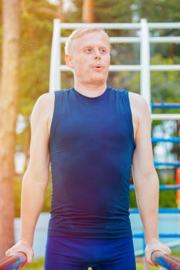 Parktaki paralel parmaklıklara triseps daldıran formda bir adam. Açık havada egzersiz yapıyor.