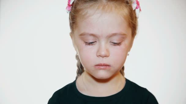 Niña comiendo piruleta naranja, luego mira a la cámara, sobre fondo blanco — Vídeos de Stock