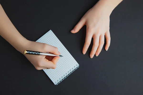 Mujer escribiendo en bloc de notas en mesa negra — Foto de Stock