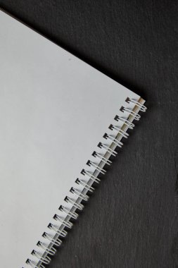 Siyah masa üstünde boş beyaz spiral defter. Üstten Görünüm.