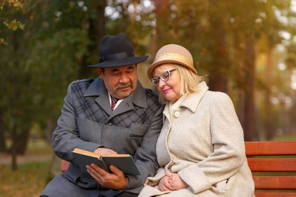 Senior couple reading book in autumn park — Stock Photo, Image