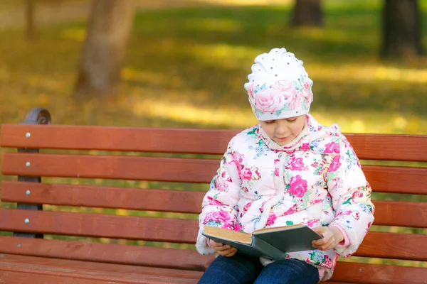 Un niño lindo está leyendo un libro en el parque . — Foto de Stock