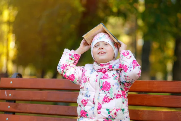 Colegiala sonriendo sosteniendo un libro en su cabeza — Foto de Stock