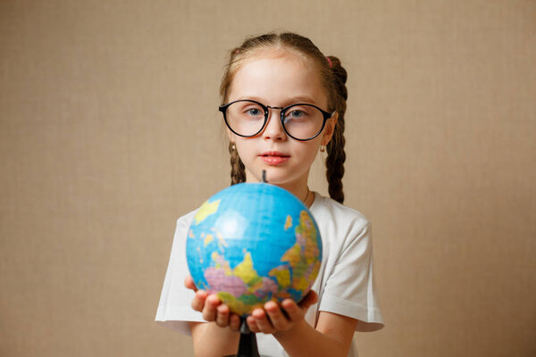 Cute little girl with globe. Child girl with glasses in white t-shirt. School Education Concept.