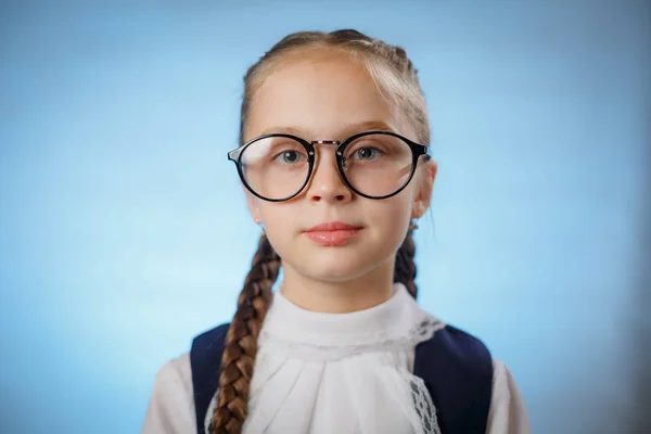 Schattig klein schoolmeisje dragen van glazen op blauwe achtergrond — Stockfoto