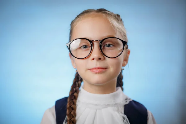 Schattig klein schoolmeisje dragen van glazen op blauwe achtergrond — Stockfoto