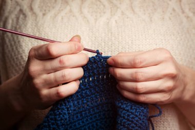 Beyaz kazaklı genç kadın örgü örüyor.