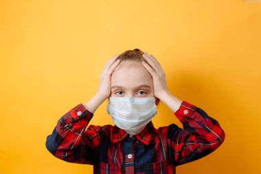 Koruyucu maskeli küçük kız sarı arka planda başını korku içinde tutuyor. Coronavirus 'a karşı koruma.