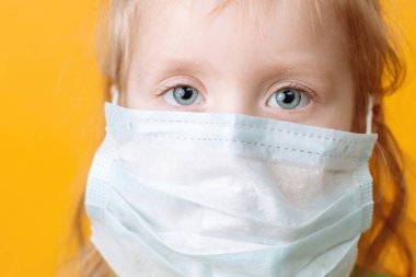 Koronavirüse karşı sarı arka planda maskeli küçük bir çocuk. Kapat.