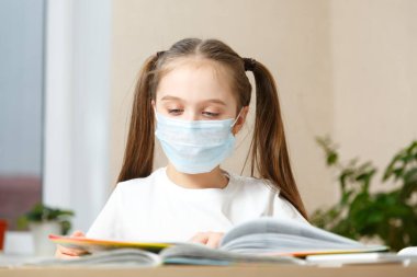 Uzak mesafede koruyucu maskeli küçük bir kız evde eğitim görüyor, karantina altında.