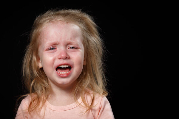 Маленькая девочка громко плачет, она очень расстроена, она истерична. Она не может успокоиться. Фото в студии на темном фоне
