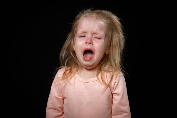 Маленькая девочка истерически плачет в темной комнате. Она сильно пострадала.
