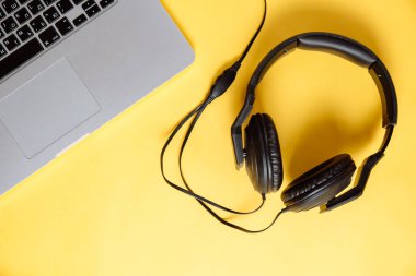 Sarı arka planda stereo kulaklıklı dizüstü bilgisayar. Düz kompozisyon. Modern aletler. Üst görünüm.