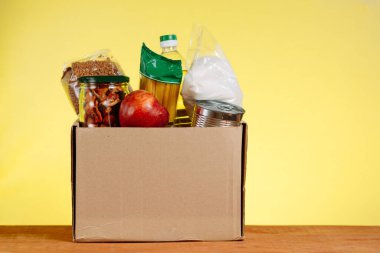 Yiyecek bağışı konsepti. Sarı arka planda bağışlanacak yiyeceklerin olduğu bağış kutusu. Coronavirüs Salgınının Bağlamında Yaşlılara Yardım.