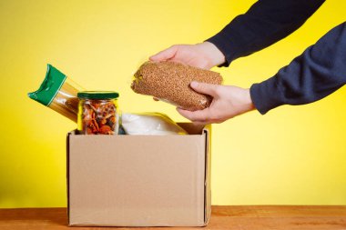 Bağış kutusunda gönüllü, sarı arka planda yiyecek var.