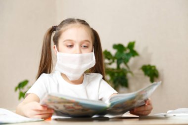 Uzaktan öğrenme çevrimiçi eğitim. Tıp maskeli hasta kız evde ders çalışıyor, okul ödevi yapıyor. Çalışma kitapları ve defterler masada.