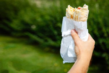 Aperatif fast food, donör, shaurma, yeşil çimlerin üzerinde bir adamın elinde.