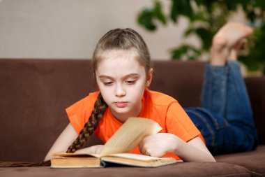 Koronavirüs yüzünden karantina sırasında evde kanepede uzanmış uzun örgü ören sevimli beyaz bir kız. Eğitim ve eğlence kavramı.