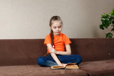 Portakal rengi tişört giyen, Lotus pozu veren, güzel, güzel, odaklanmış, neşeli genç bir kızın portresi.