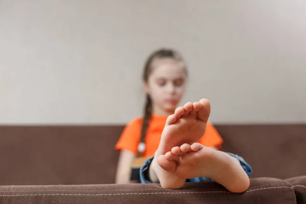 Evdeki bir kanepede otururken çıplak ayakla kitap okuyan beyaz bir kız. Ayak yakın plan. seçici odak.