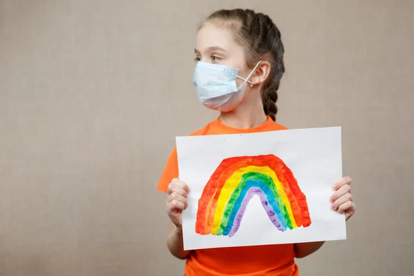 A child shows a drawing of a rainbow during pandemic coronavirus quarantine. Stay at home Social media campaign for coronavirus prevention, let's all be well, hope during coronavirus pandemic concept.