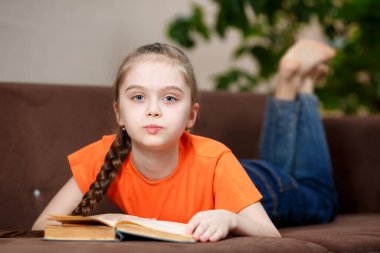 Koronavirüs yüzünden karantina sırasında evde kanepede uzanmış uzun örgü ören sevimli beyaz bir kız. Eğitim ve eğlence kavramı.