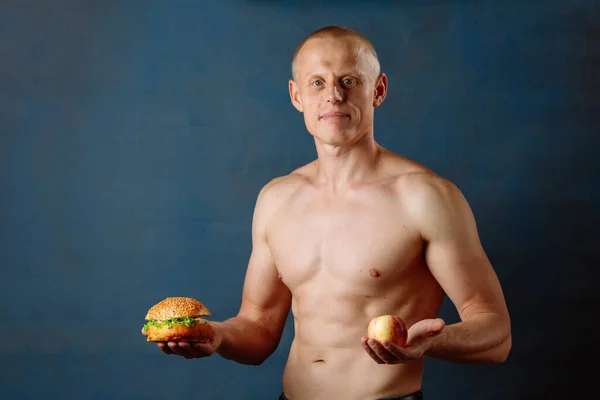 Athlete Man chooses between a hamburger and an apple. The concept of choosing the right food.